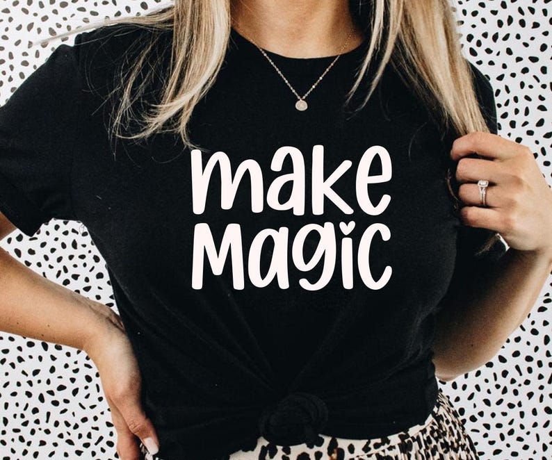 May include: Black t-shirt with the words "make magic" in white script. The shirt is knotted at the waist. The background is a black and white spotted pattern.