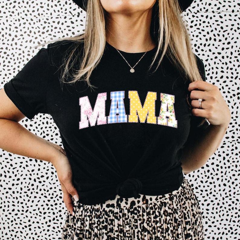 May include: Black t-shirt with the word "MAMA" in colorful patchwork letters. The letters are in floral, gingham, and yellow patterns. The shirt is knotted at the waist and paired with a leopard print skirt.