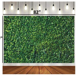 May include: A green foliage backdrop, 82 inches wide and 59 inches high, with a wooden floor and string lights. The backdrop is covered in dense, vibrant green leaves, creating a natural, textured appearance. The lights hang from above, adding a decorative touch.