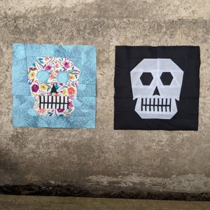 May include: Two fabric squares featuring a skull design. One square is blue with a floral skull design. The other square is black with a white skull design.