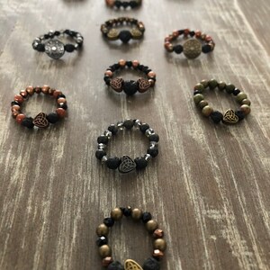 Puede incluir: Una colecci&oacute;n de diez pulseras de cuentas con cuentas de roca volc&aacute;nica y un dije de nudo celta. Las pulseras son de varios colores, incluyendo negro, marr&oacute;n, verde y plateado.
