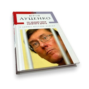 May include: A white book with a red title bar. The title is "Yuriy Lutsenko" in black text. The subtitle is "Po obidva boki kol'ochogo drotu" in smaller black text. The book cover features a close-up photo of a man with glasses looking directly at the camera.