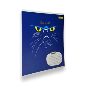 May include: A blue notebook with a black cat illustration and the text "Khana katam!" in yellow letters. The notebook has a white border and a yellow and blue sticker.
