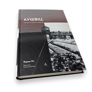 May include: A black and white book cover with the title "AUSCHWITZ" in white text. The cover features a black and white photograph of a train track leading to a gate with a building in the background. The book is by Lorenz Pic and translated by Anastasia Shymbal.