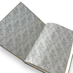 May include: An open book with a floral pattern on the cover and pages. The pattern is a repeating design of gray flowers on a white background.