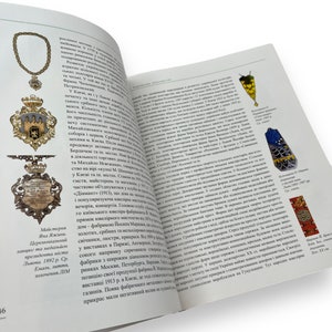 May include: A gold-colored pendant with a detailed design of a coat of arms. The pendant is suspended from a chain and features a red and white shield with a lion and a crown. The pendant is surrounded by a decorative border.
