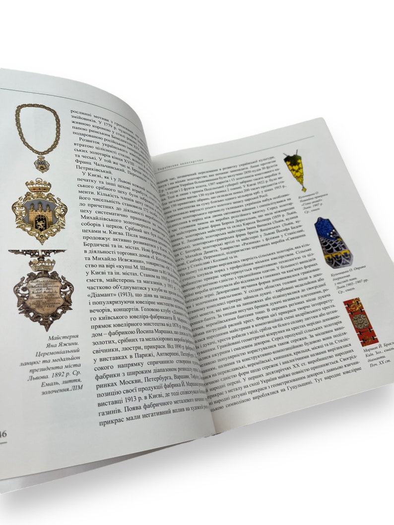 May include: A gold-colored pendant with a detailed design of a coat of arms. The pendant is suspended from a chain and features a red and white shield with a lion and a crown. The pendant is surrounded by a decorative border.