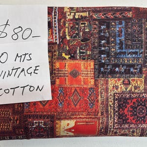 May include: Vintage cotton fabric with a patchwork design in shades of red, orange, and brown. The fabric features intricate patterns reminiscent of antique rugs. The handwritten label reads "10 mts VINTAGE COTTON."