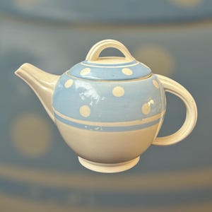 May include: A blue and white teapot with white polka dots. The teapot has a round body and a spout on the side. The teapot is made of ceramic.