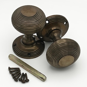 May include: Antique bronze door knobs with a ribbed design. The set includes two knobs, backplates, screws, and a metal tool. The knobs have a classic, vintage aesthetic, suitable for interior doors. The hardware is made of metal.