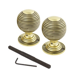 May include: Two brass-effect, spherical door knobs with black horizontal stripes. Each knob sits on a circular base with concentric grooves. A long, threaded rod and an Allen key are included.