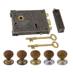 May include: An antique-style door lock set with a decorative, dark grey metal lock, two brass keys, and five wooden door knobs with brass and silver-toned bases. The lock features ornate scrollwork.