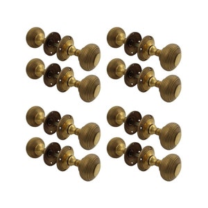 May include: Eight antique brass door knobs with a ribbed design. Each knob has a round shape and is mounted on a circular backplate. The knobs are arranged in two rows of four, against a white background.