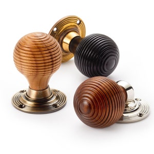 May include: Three decorative door knobs in a close-up shot. One is light brown, one is black, and one is dark brown. Each knob has a round, ribbed design. The bases are brass, nickel, and bronze.