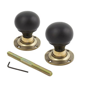 May include: A pair of black spherical door knobs with brass-toned bases, a threaded rod, and a hex key. The door knobs have a classic design. The bases have a circular design and are likely for interior doors.