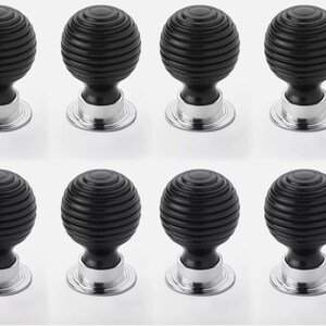 May include: Eight black cabinet knobs with a grooved, spherical design. Each knob has a silver-coloured base. These decorative knobs are suitable for drawers, cabinets, or furniture.