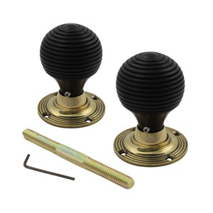 May include: A pair of black, ribbed door knobs with brass-coloured bases, a bolt and an Allen key. The spherical knobs are designed for a classic or vintage look. The circular bases feature concentric grooves, suitable for interior doors.