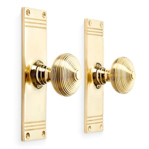 May include: Two polished brass door handle sets. Each set features a rectangular backplate with horizontal lines and a round, grooved doorknob. The hardware is set against a white background.