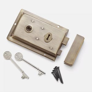 May include: A vintage-style brass door lock set. The set includes a rectangular lock body, a separate latch, two ornate keys, and a small pile of black screws. The lock and latch have a weathered finish.