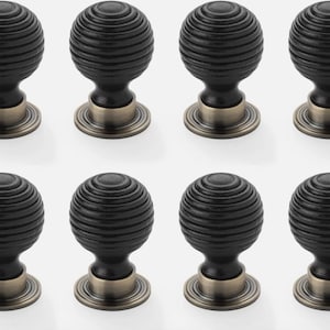 May include: Eight black ribbed cabinet knobs with a bronze-coloured base. The knobs have a round, ball-like shape with horizontal grooves. The hardware is designed for use on drawers or cabinets.