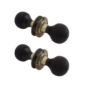 May include: Two antique door knobs. Each has a dark, ribbed, spherical handle and a circular, aged brass base. The knobs are designed for a classic or vintage aesthetic, suitable for period properties.