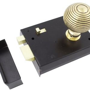 May include: A black mortise lock with a brass-coloured, spherical doorknob. The lock has a rectangular shape with a matching black strike plate. The doorknob features a grooved design.