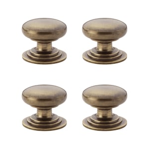May include: Four antique brass cabinet knobs. Each knob features a rounded top, a short stem, and a tiered base. The knobs are a warm, metallic colour, and are arranged in a square formation against a white background.