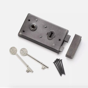 May include: A dark grey mortise lock with two silver keys. The lock has a keyhole and is accompanied by a matching strike plate and a set of black screws. The keys have decorative circular tops.
