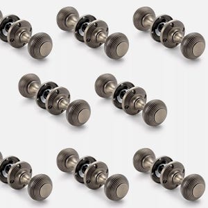 May include: Nine antique-style door knobs with a ribbed, rounded design. The knobs are a muted silver colour and appear to be made of metal. Each knob has a circular backplate and a black centre. The knobs are arranged in a grid pattern.