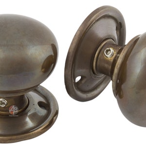 Peut inclure: Deux poign&eacute;es de porte de style antique avec une finition bronze. Chaque bouton a une forme ovale et est mont&eacute; sur une plaque arri&egrave;re ronde. La quincaillerie est en m&eacute;tal et a une esth&eacute;tique vintage.