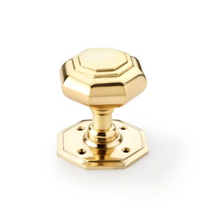 May include: A polished brass door knob with an octagonal design. The knob has a multi-faceted head and a matching octagonal base with screw holes. The hardware is a bright gold colour and is set against a white background.
