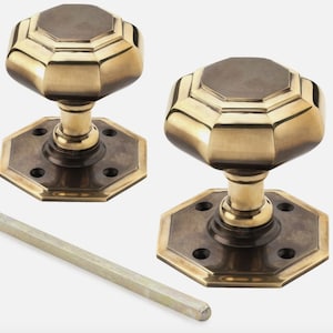 May include: Two antique brass door knobs with an octagonal design. Each knob has a dark centre and sits on a hexagonal base. A metal rod is included. Suitable for interior doors.
