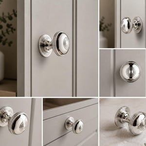 May include: A selection of polished silver cabinet knobs with a circular design. The knobs are mounted on a light grey cabinet door and drawer fronts. The knobs have a decorative base and a rounded, ridged centre. The image showcases the knobs in various angles and close-ups.