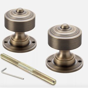 May include: Two antique brass door knobs with a ridged design. The knobs have a circular base and a cylindrical top. A long screw and an Allen key are included.