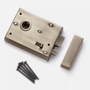 May include: A bronze-finished door lock set, comprising the main lock body, a separate latch, and a set of dark screws. The lock has a rectangular shape with rounded edges and several screw holes. A classic design.