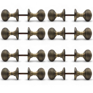 May include: Twelve antique brass door knobs with a ribbed design. Each knob is connected by a metal rod. The knobs are arranged in a grid pattern against a white background. The hardware has a vintage aesthetic.
