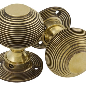 May include: A pair of antique brass door knobs. Each knob has a spherical shape with a ribbed, concentric design. The brass has a warm, golden colour. The knobs are mounted on circular backplates, offering a classic aesthetic.
