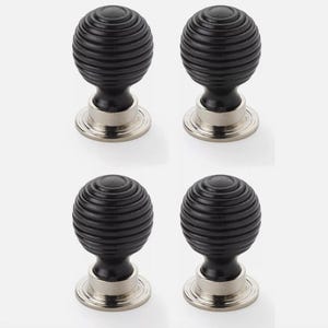 May include: Four black cabinet knobs with a round, ribbed design. Each knob has a silver-coloured base. The knobs are arranged in a square formation against a white background.