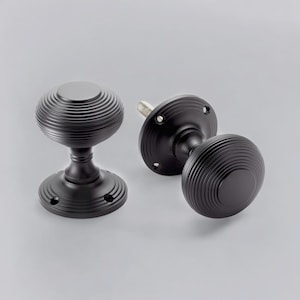 May include: Two black door knobs with a circular, grooved design. The knobs have a round base and a cylindrical stem. The hardware is made of metal and has a matte finish. The door knobs are for interior use.