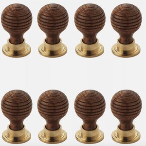 May include: Eight wooden cabinet knobs with a grooved, spherical design. The knobs are a warm brown colour and sit atop a brass-coloured base. The knobs are arranged in two rows of four.