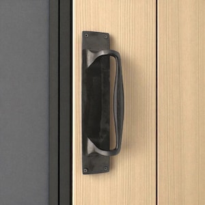 May include: A black metal door pull with a curved handle, fixed to a light wood door. The door pull is rectangular and has a matte finish. The door is next to a dark grey door.
