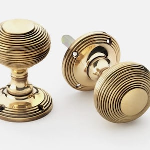 May include: Three brass door knobs with a spiral design. The knobs are a warm gold colour and have a round shape. One knob is attached to a circular base, and the other two are separate.