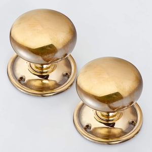 May include: A pair of polished brass door knobs. Each knob has a rounded, dome-like shape and sits on a circular base with screw holes. The brass has a warm, golden colour, reflecting light.