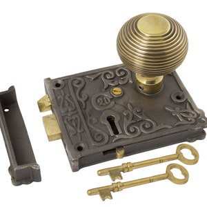May include: An antique door lock set with a bronze finish. The set includes a decorative lock plate with ornate detailing, a brass doorknob, a strike plate, and two skeleton keys. The lock plate has the number 20 engraved on it.