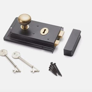 May include: A black door latch with a brass knob and keyhole, alongside two keys and a strike plate. The rectangular latch is designed for door security. Includes mounting hardware.