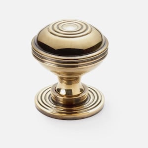 May include: A brass door knob with a round, ridged design. The knob has a circular base and a spherical top with concentric rings. The hardware is a warm gold colour and is suitable for interior doors.