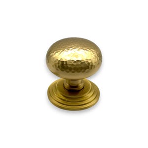 May include: A gold cabinet knob with a hammered texture on the round handle. The knob sits on a circular base with concentric rings. The hardware is designed for use on cabinets, drawers, or furniture.