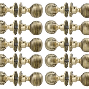 May include: Ten brass door knobs, each with a ribbed, spherical design and a circular backplate. The knobs are arranged in two rows of five against a white backdrop. The overall aesthetic is vintage.