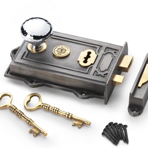 May include: A detailed image of a vintage door lock set. The set includes a silver and gold lock, two ornate gold keys, and a matching strike plate. The lock features a hammered silver knob and decorative accents.
