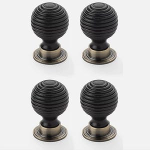 May include: Four black, ribbed cabinet knobs with a bronze-coloured base. The knobs are spherical with horizontal grooves, creating a textured appearance. The base has a circular design.